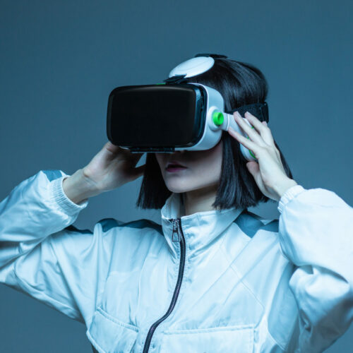 Excited young woman having virtual reality experience in neon light